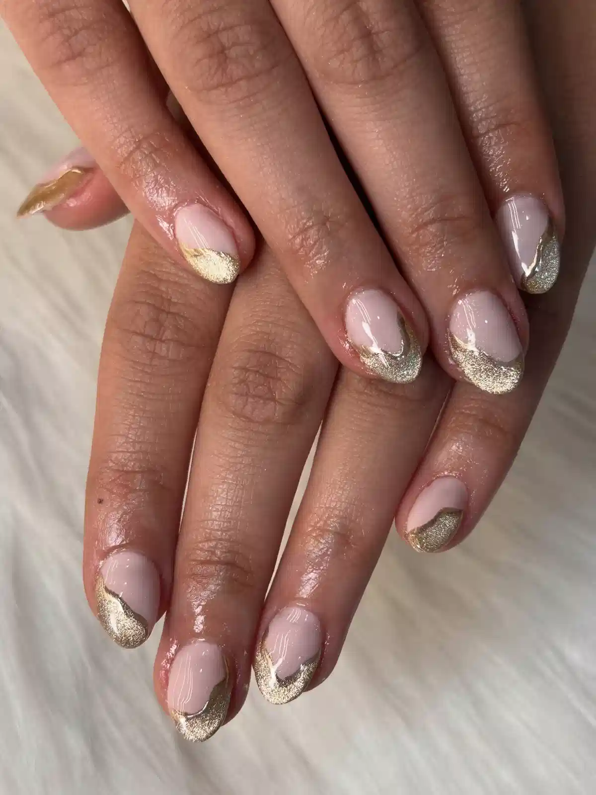 Short nude nails with curved gold glitter French tips