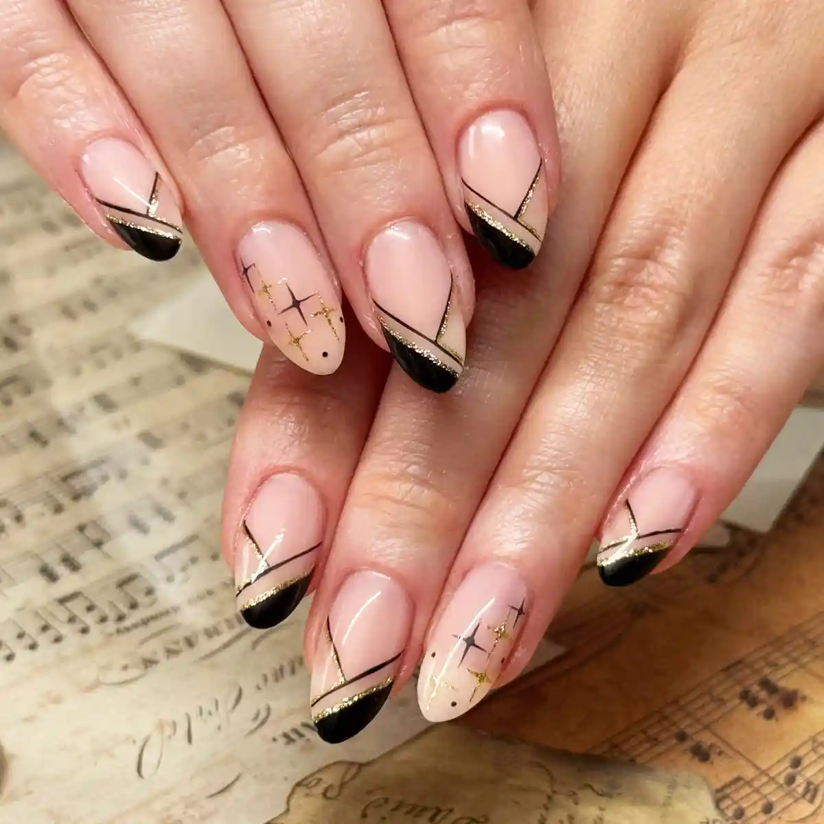 Nude nails with black tips, gold striping, and starburst accents