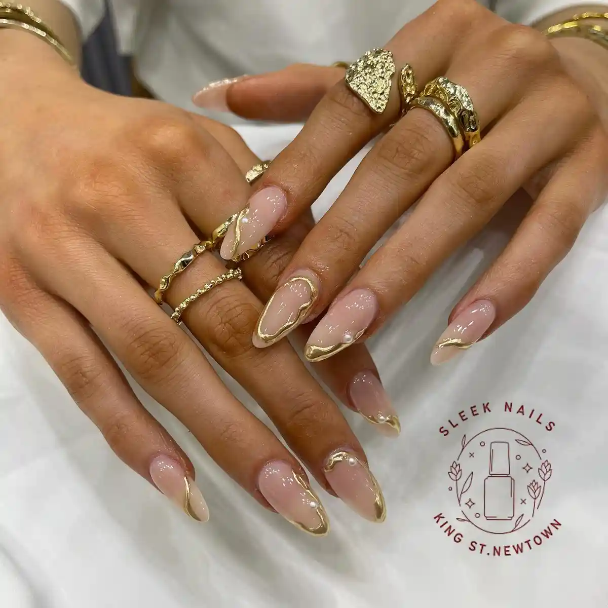 Glossy nude almond nails with flowing gold edges and bead accents