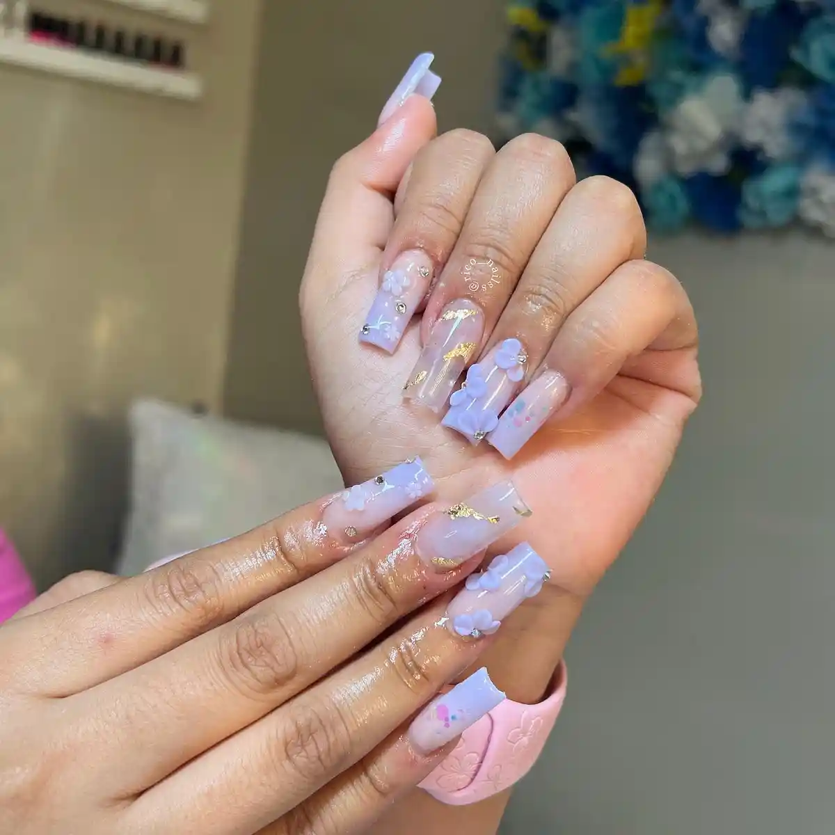 Long lavender French tips with 3D flowers, rhinestones, and gold flakes
