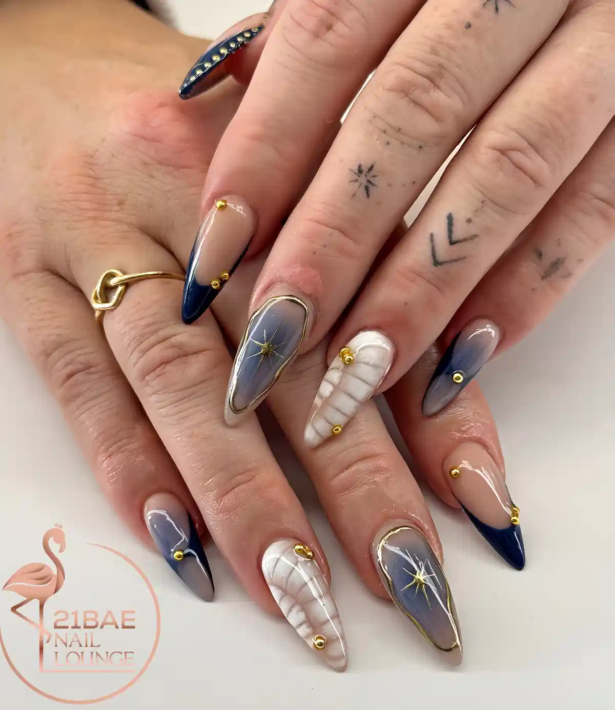 Stiletto nails in navy and gray-blue with gold outlines and starburst accents