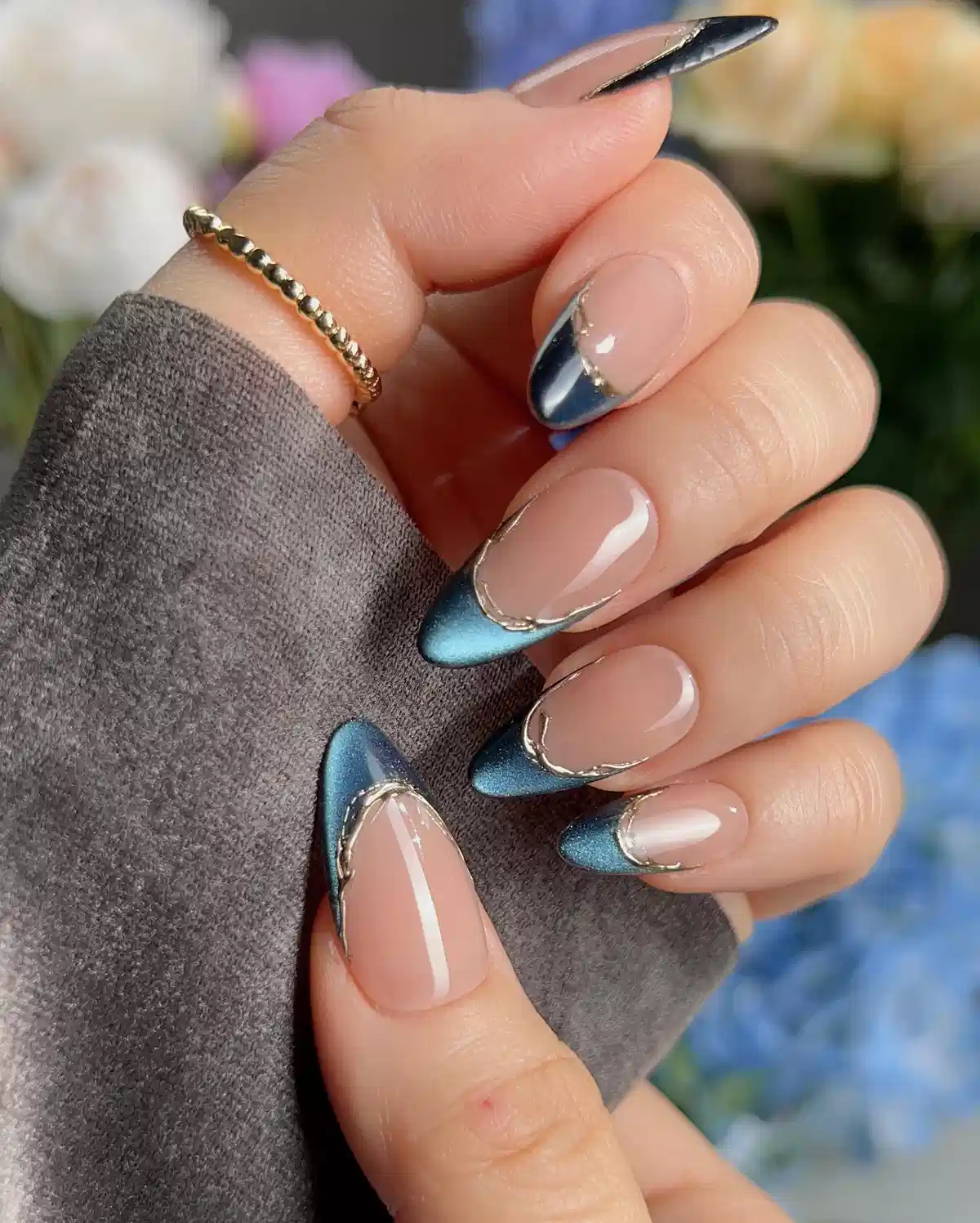 Nude nails with teal-blue metallic French tips and gold outlining