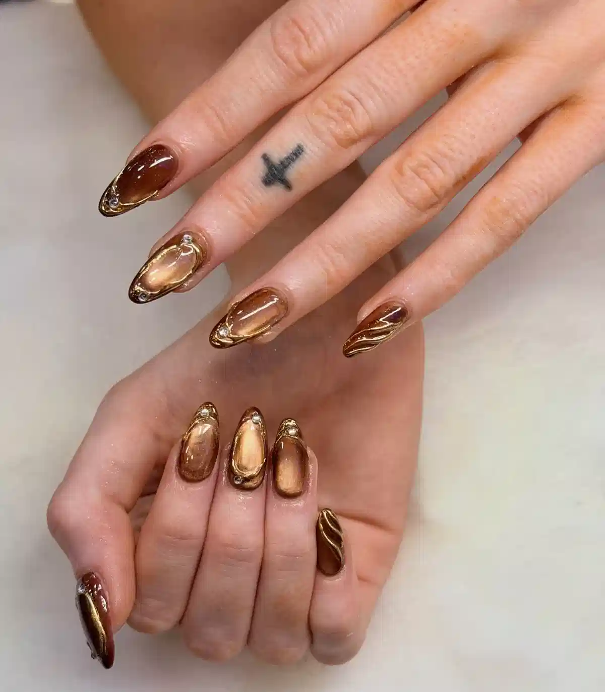 Brown-and-gold framed almond nails with small gem accents