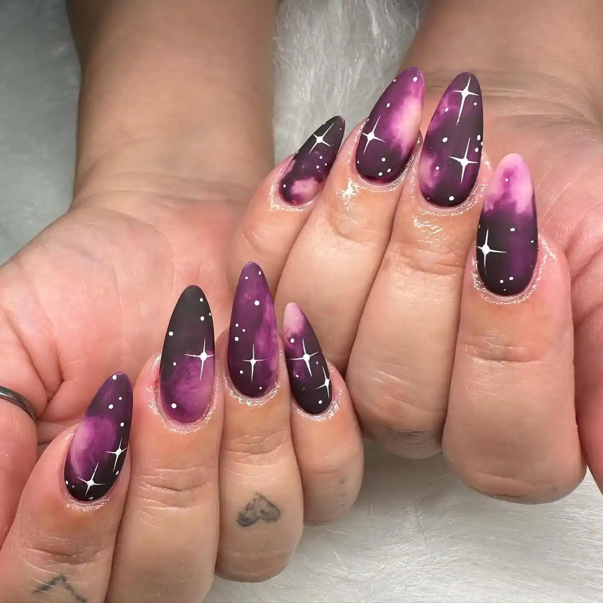 Dark purple galaxy-style nails with stars and dots
