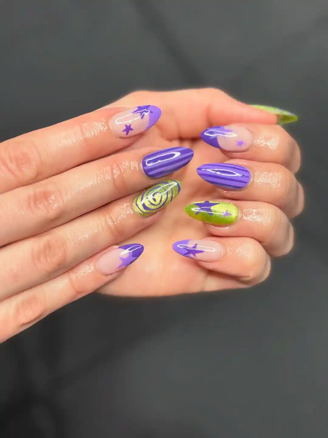 Purple tips, stars, and striped accents with a green swirl nail