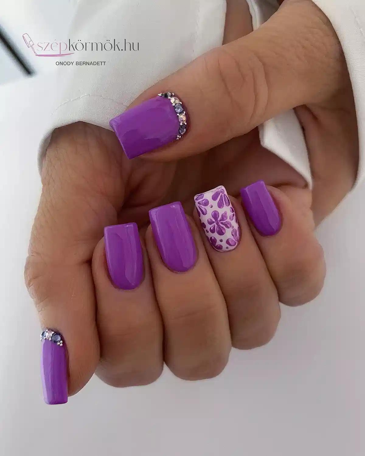 Solid purple squares with a white floral accent and gem cuticle arcs