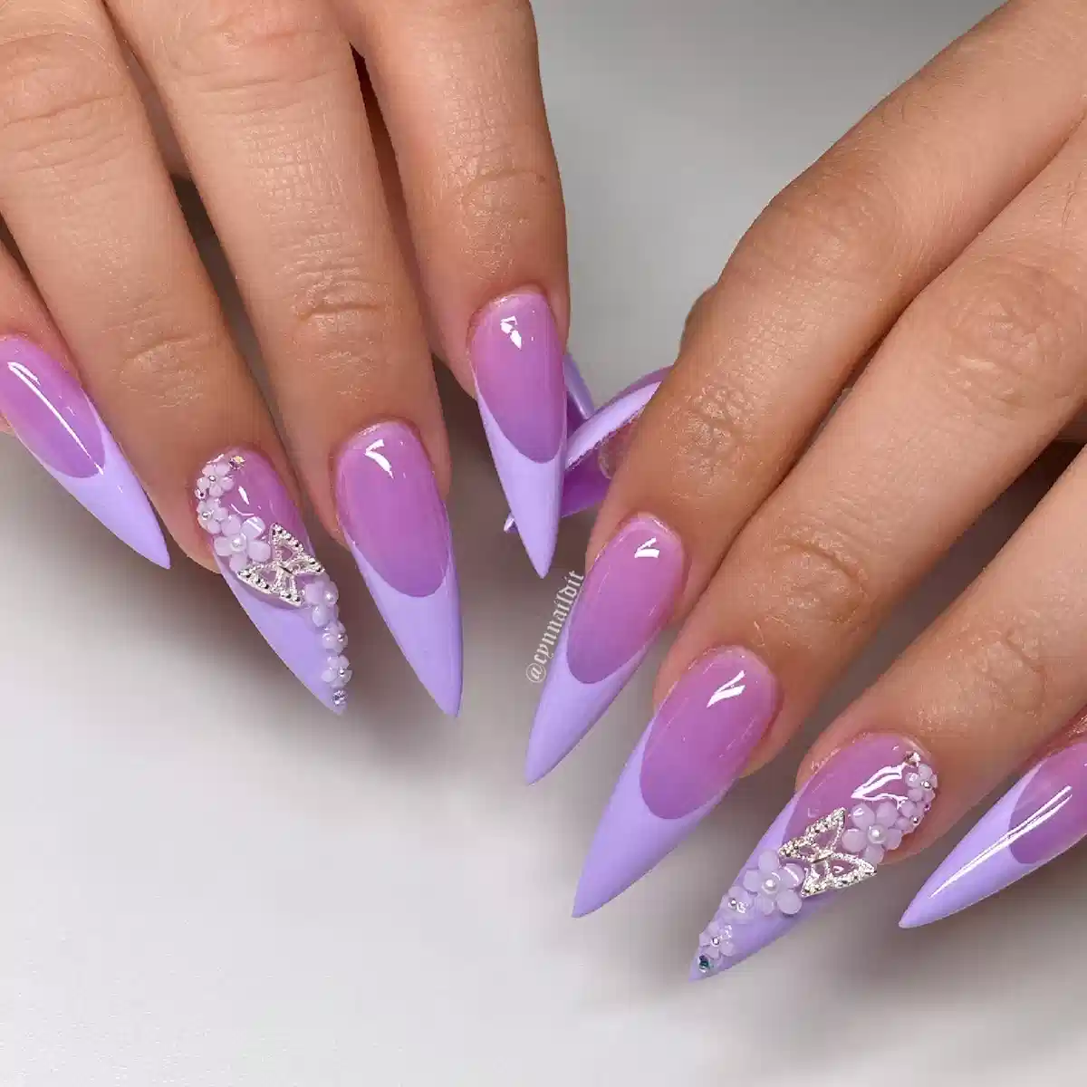Lavender stiletto nails with purple insets and rhinestone clusters