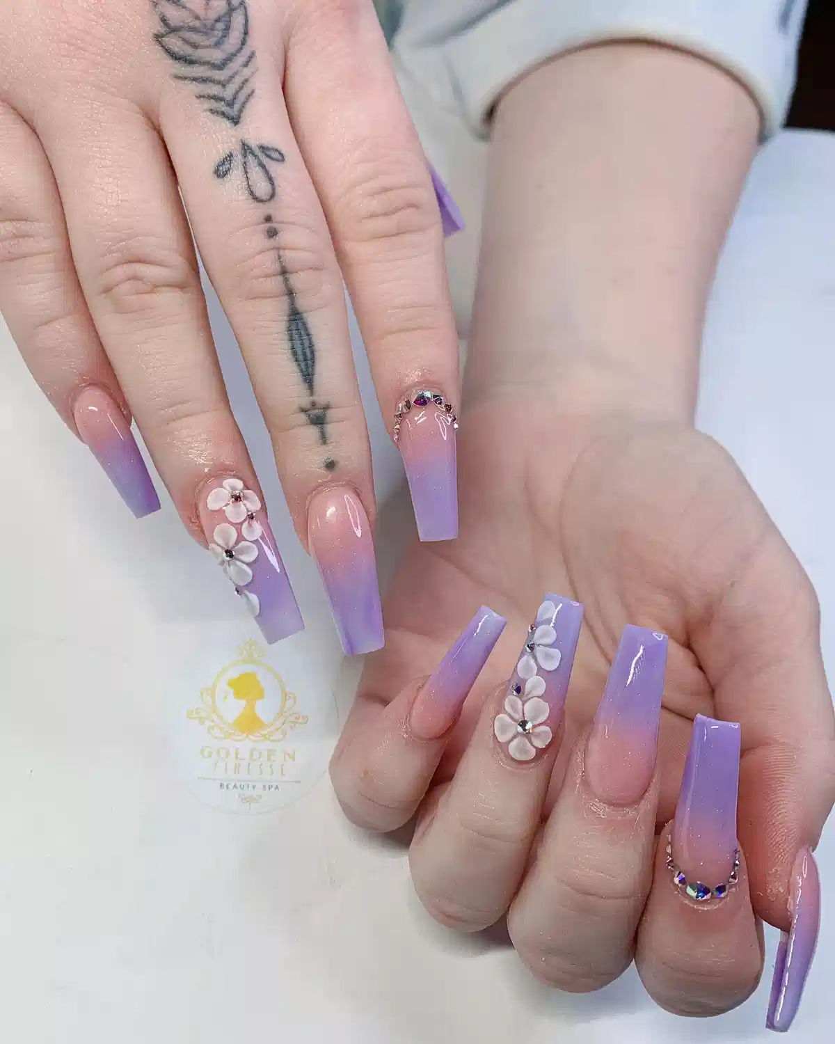 Nude-to-lavender ombré coffin nails with 3D white flowers and rhinestones