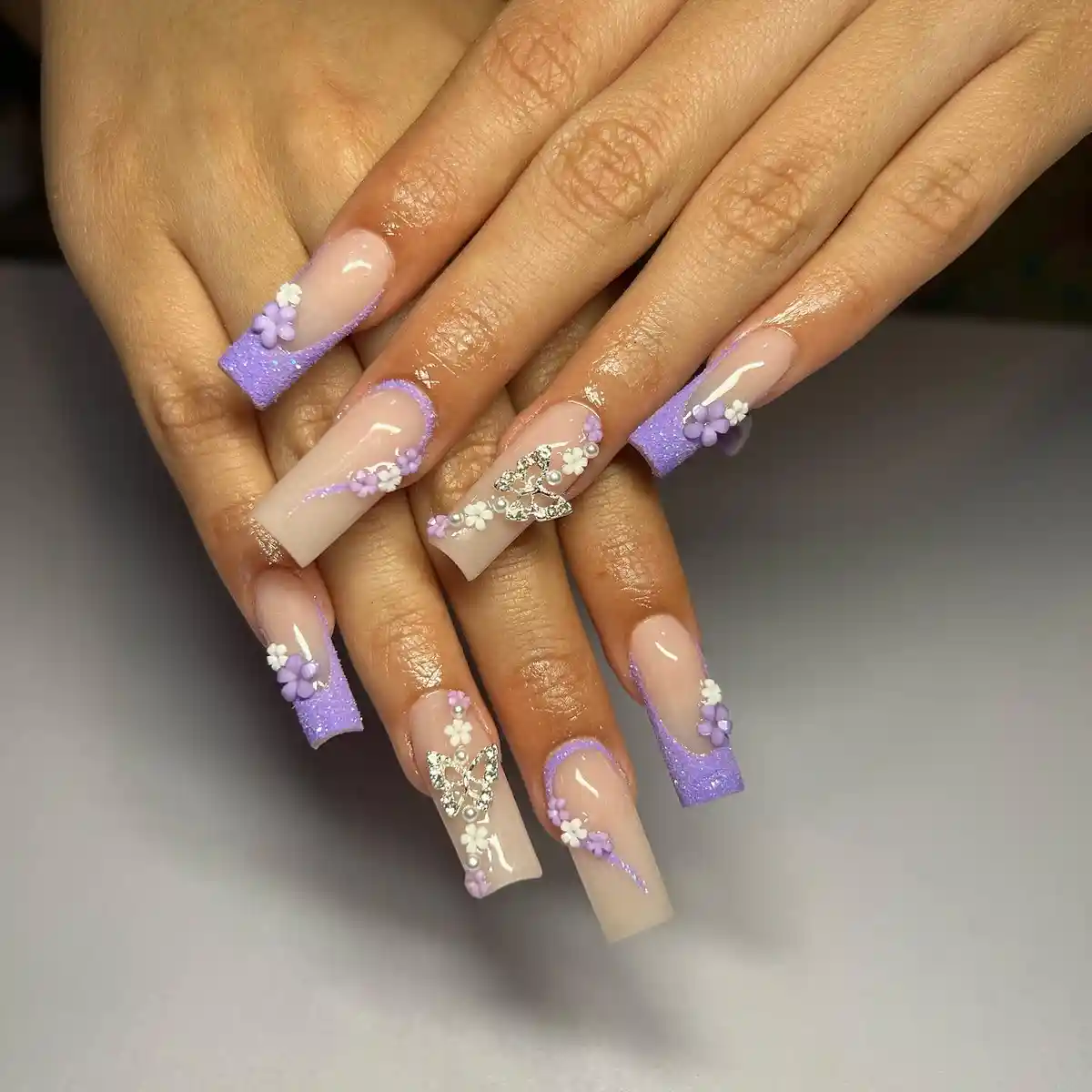 Lavender glitter French tips with 3D florals and rhinestone butterflies