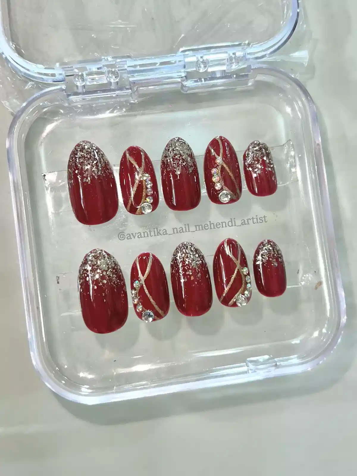 Deep red glitter-cuticle press-ons with gold diagonals and rhinestones