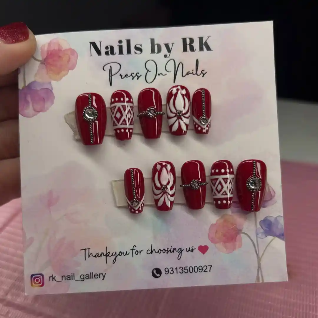 Red press-ons with white patterns and silver-toned chain embellishments