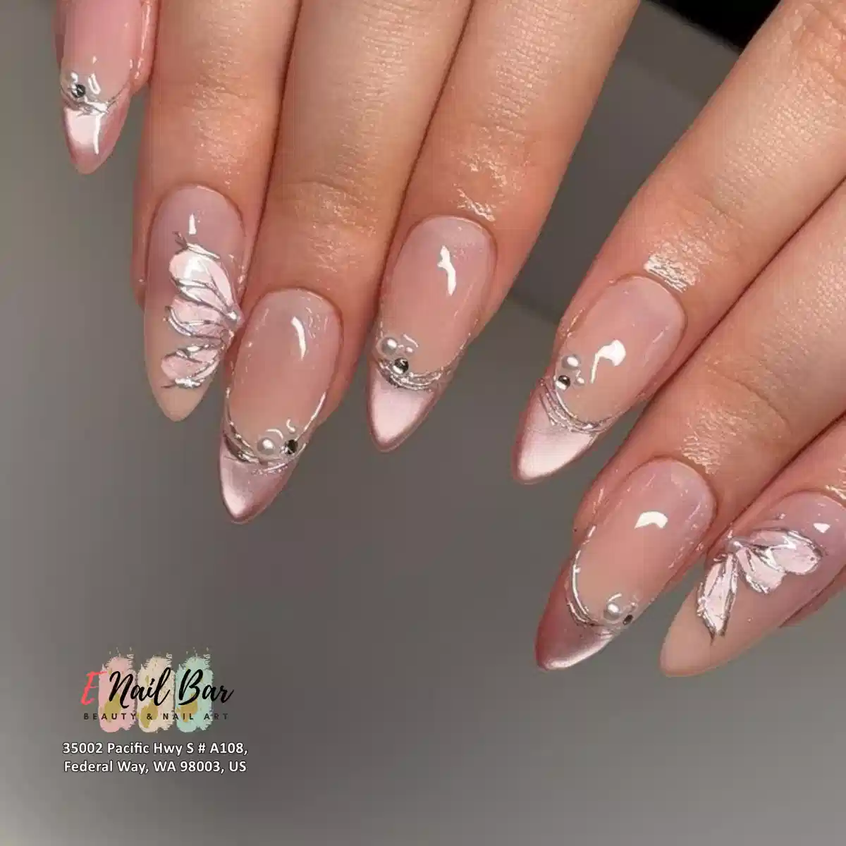 Nude-pink almond nails with pale tips, silver lines, and pearl accents