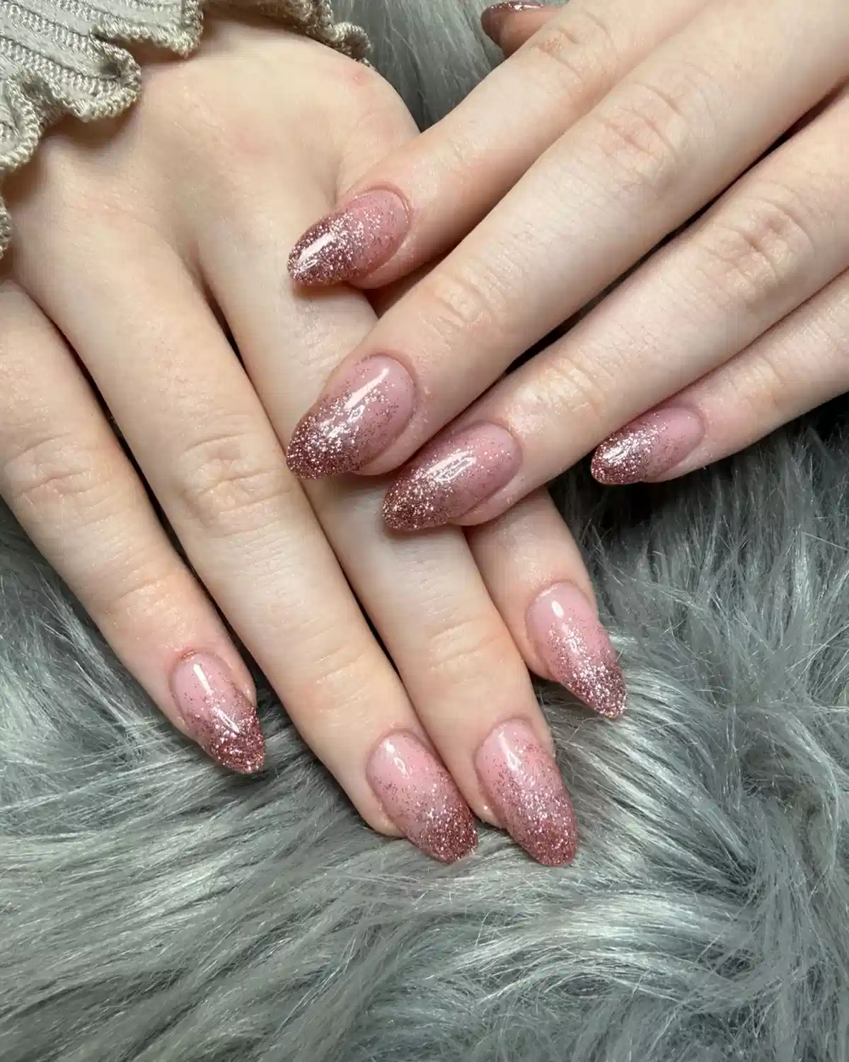 Pale pink almond nails with rose-gold glitter fade at the tips