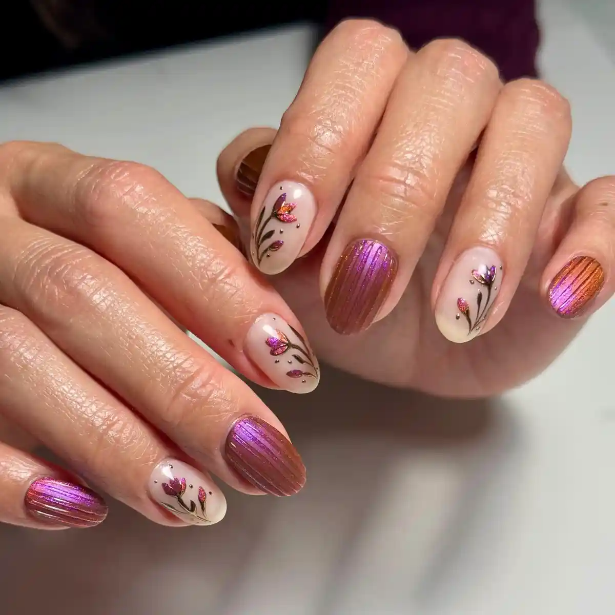 Metallic purple/orange textured nails with floral nude accents