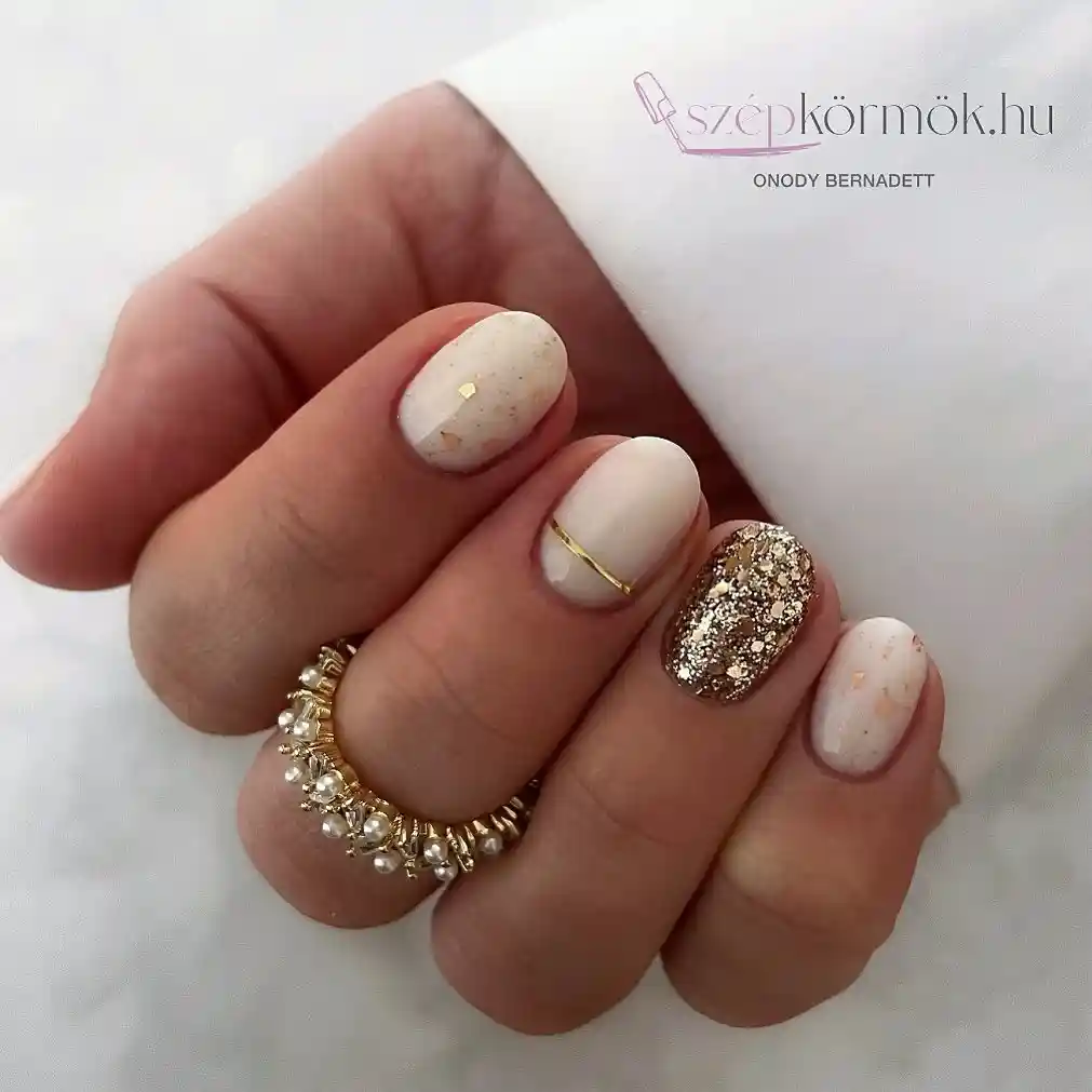 Short off-white speckled nails with gold glitter accent